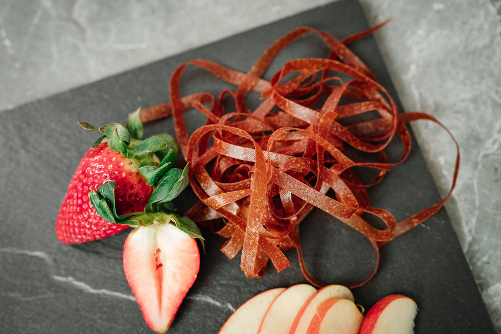Auf einer Schieferplatte liegen Erdbeeren, Fruchtschlangen Sorte Erdbeere sowie Apfelschnitze