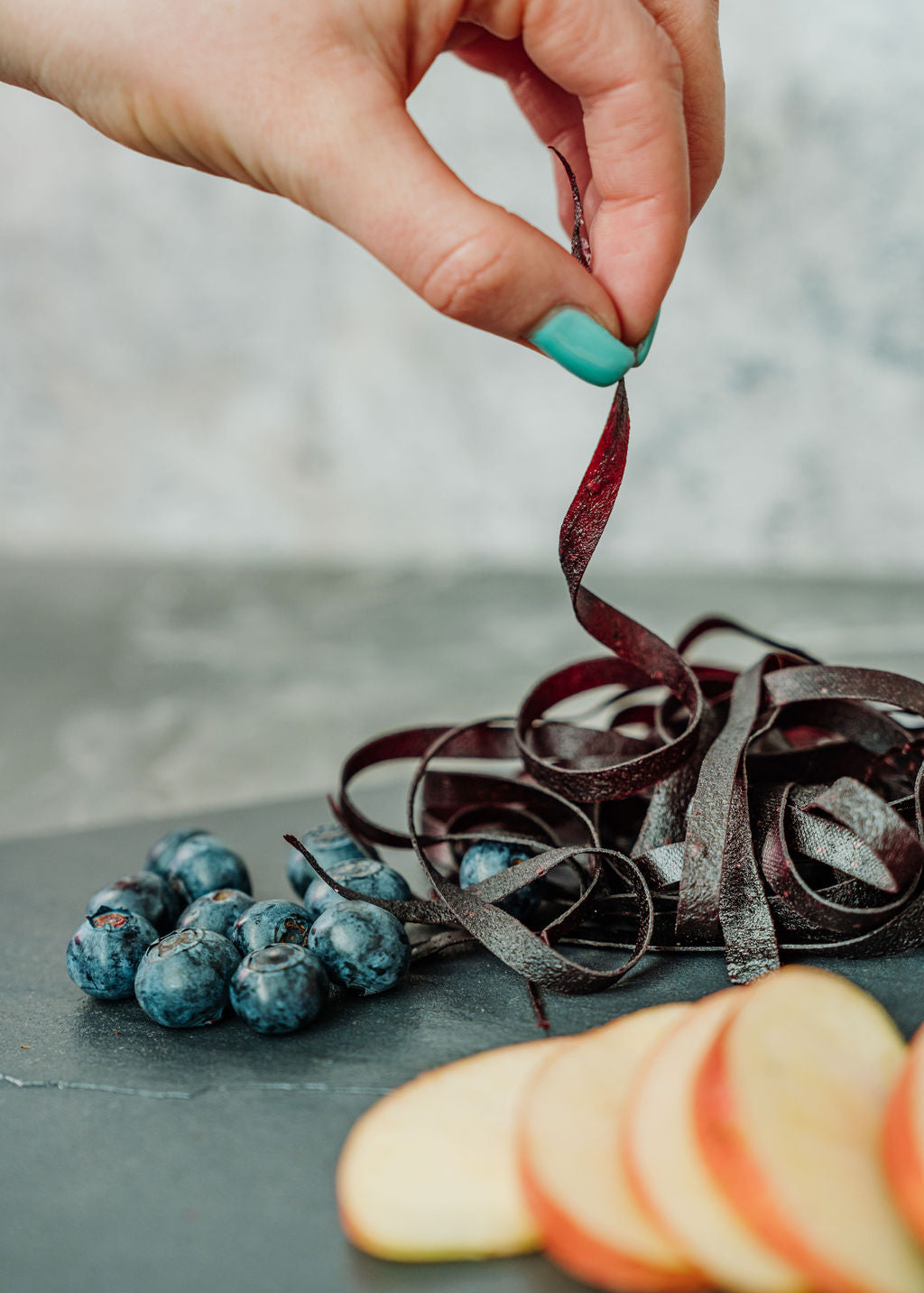 Fruchtschnüre Heidelbeere mit Früchten Äpfel und Heidelbeere auf Schieferplatte. Hand greift nach Fruchtschnüren