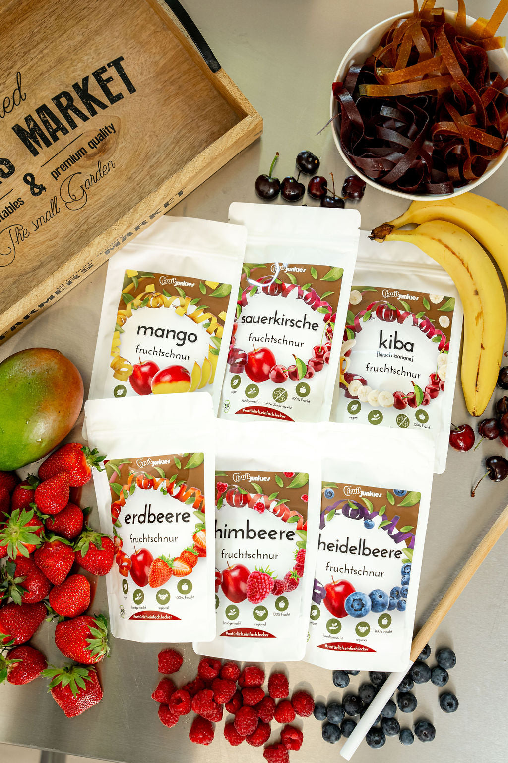 Fruchtschlangentüten fruitjunkies 36g Mango, Sauerkirsche, KiBa, Erdbeere, Himbeere, Heidelbeere sowie Fruchtschlangen in einer Schale, Sauerkirschen, Bananen, Heidelbeeren, Himbeeren, Erdbeeren und Mango