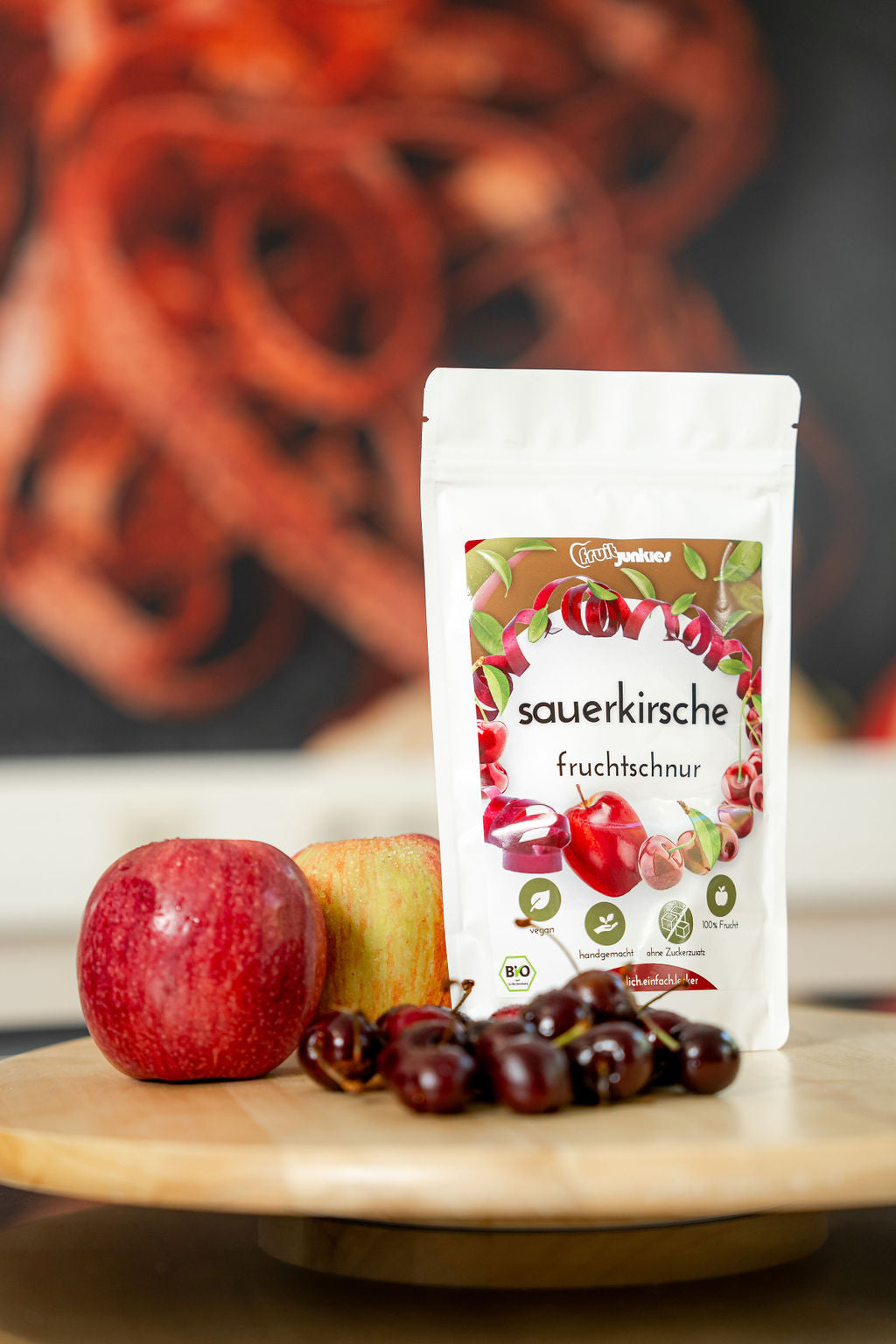 36g Fruchtschnurtüte Sorte Sauerkirsche auf einem Holzteller mit Apfel und Sauerkirsche