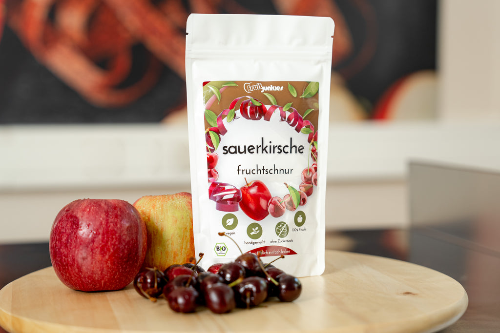 36g Sauerkirsch Tüte von fruitjunkies auf Holzdrehteller mit umliegenden Früchten Äpfel und Sauerkirsche